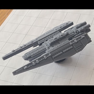 May include: A grey plastic spaceship model with intricate detailing. The model features a long, streamlined design with multiple sections and protruding elements. It is set against a grid background.