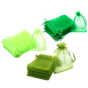 May include: A set of green and lime green organza gift bags. The bags are made of sheer fabric and are tied with a ribbon. The bags are stacked on top of each other.