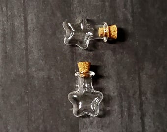 Può includere: Due piccole bottiglie di vetro a forma di stella con tappi di sughero. Le bottiglie sono trasparenti e vuote.