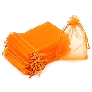 May include: A stack of 25 orange sheer organza gift bags. The bags are made of a delicate, lightweight fabric and have a drawstring closure.