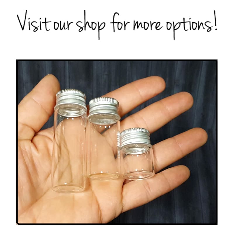 May include: Three clear glass bottles with silver lids. The bottles are different sizes and are held in a hand.