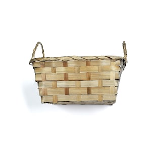 May include: A rectangular woven basket with two handles. The basket is made of light brown and tan woven material. The basket is empty and sits on a white background. The basket is a natural, rustic style.