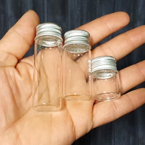 May include: Three clear glass bottles with silver lids of varying sizes. The bottles are empty and have a smooth, cylindrical shape.