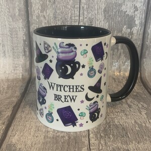 May include: White ceramic mug with a black handle and black rim. The mug has a design of various witchy items, including a cauldron, a witch's hat, a crescent moon, and stars. The text "Witches Brew" is printed on the mug.