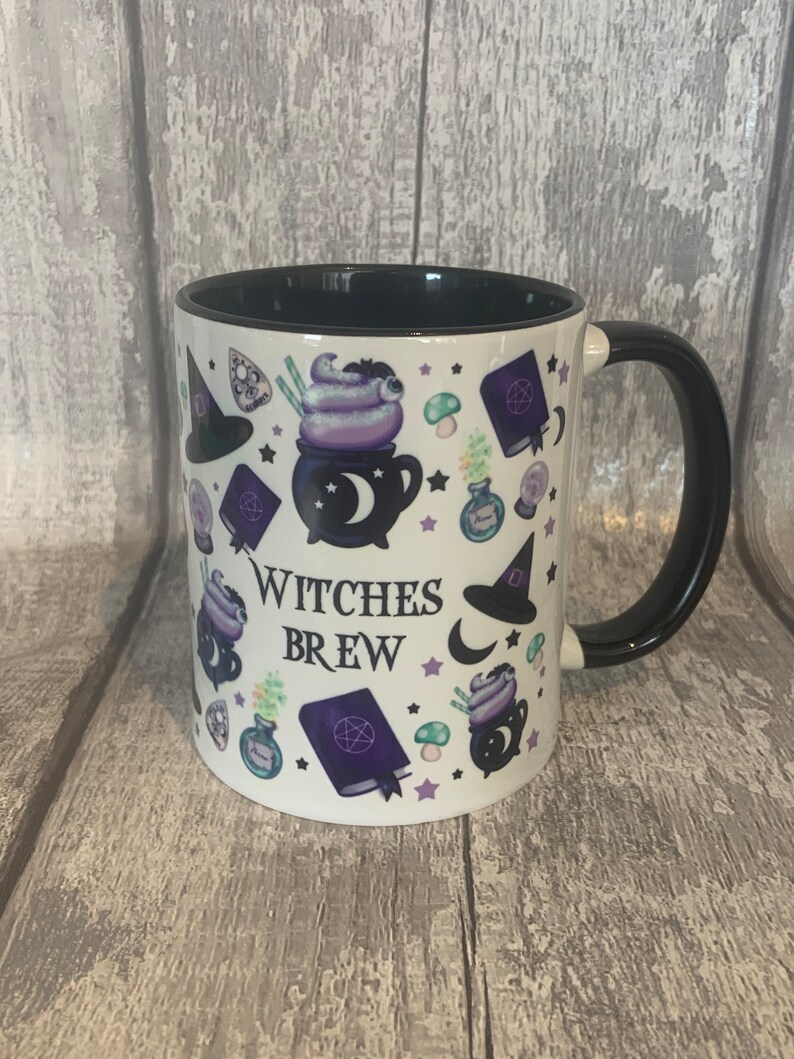 May include: White ceramic mug with a black handle and black rim. The mug has a design of various witchy items, including a cauldron, a witch's hat, a crescent moon, and stars. The text "Witches Brew" is printed on the mug.