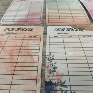 May include: A collection of rectangular cash tracker cards with various watercolor backgrounds in pink, peach, and blue hues. Each card features a grid for tracking expenses, with the words "Cash Tracker" and fields for "Date," "+/-," and "New Total."
