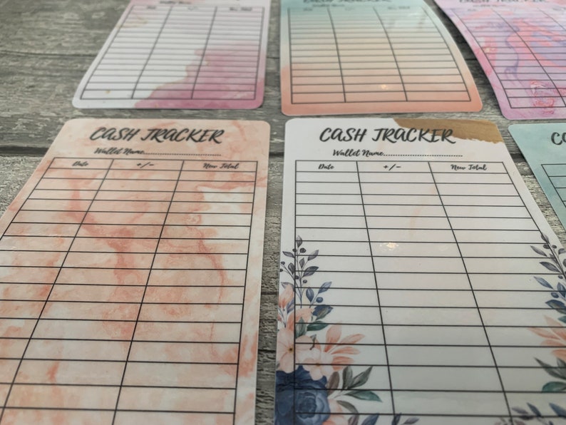 May include: A collection of rectangular cash tracker cards with various watercolor backgrounds in pink, peach, and blue hues. Each card features a grid for tracking expenses, with the words "Cash Tracker" and fields for "Date," "+/-," and "New Total."