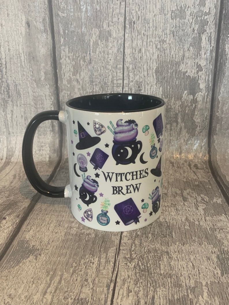 May include: White ceramic mug with a black handle and a black rim. The mug has a design of a cauldron, a witch's hat, stars, and other witchy elements. The text "Witches Brew" is printed on the mug.