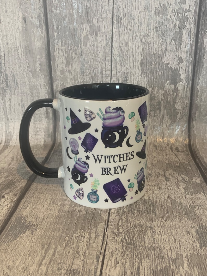 May include: White ceramic mug with a black handle. The mug has a black rim and features a white background with a black and purple design of a cauldron, stars, a witch's hat, and the text "Witches Brew".