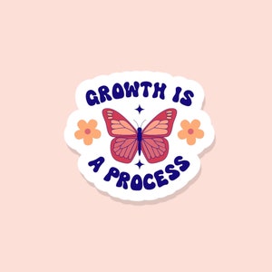 May include: A white sticker with a blue and white text that says "Growth is a process" and a pink butterfly with two yellow flowers on either side.