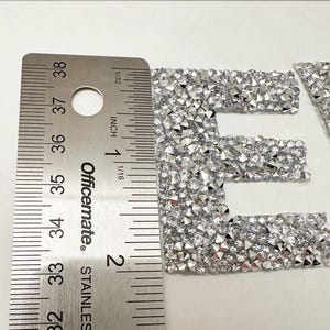 May include: Close-up of a silver letter "E" made of rhinestones. The letter is approximately 1 inch tall and is measured with a ruler.