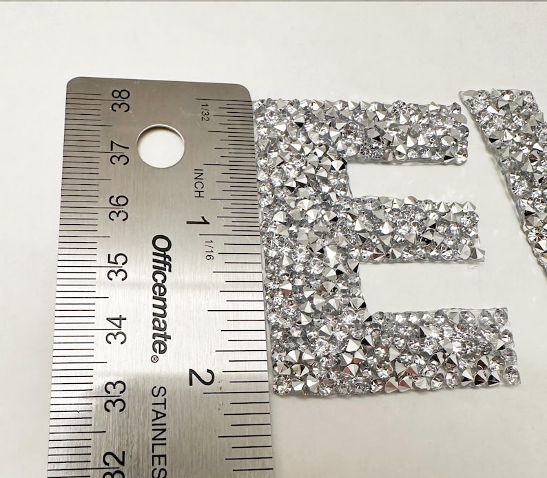 May include: Close-up of a silver letter "E" made of rhinestones. The letter is approximately 1 inch tall and is measured with a ruler.