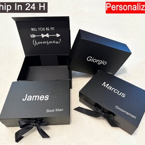 Puede incluir: Tres cajas de regalo negras con texto blanco. La caja superior est&aacute; abierta y dice "&iquest;Quieres ser mi padrino?" con una flecha y una corbata de lazo. Las otras cajas dicen "James Mejor Hombre", "Giorgio" y "Marcus Padrino".