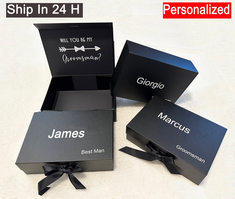 Puede incluir: Tres cajas de regalo negras con texto blanco. La caja superior est&aacute; abierta y dice "&iquest;Quieres ser mi padrino?" con una flecha y una corbata de lazo. Las otras cajas dicen "James Mejor Hombre", "Giorgio" y "Marcus Padrino".