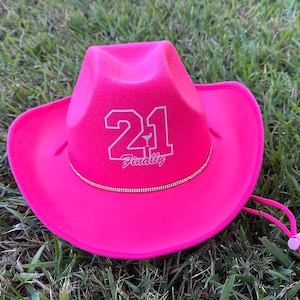 Peut inclure: Un chapeau de cowboy rose vif avec un design en feutre blanc qui dit "21 Enfin" avec un petit graphique de verre &agrave; cocktail.
