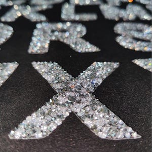 May include: A close-up of a black fabric with the letter "X" made of small, clear rhinestones.