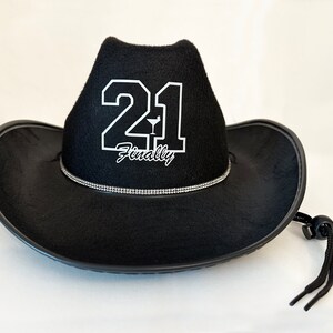 Peut inclure: Chapeau de cowboy noir avec une applique en feutre blanc du num&eacute;ro 21 et le mot "Enfin" avec une petite ic&ocirc;ne de verre &agrave; martini.
