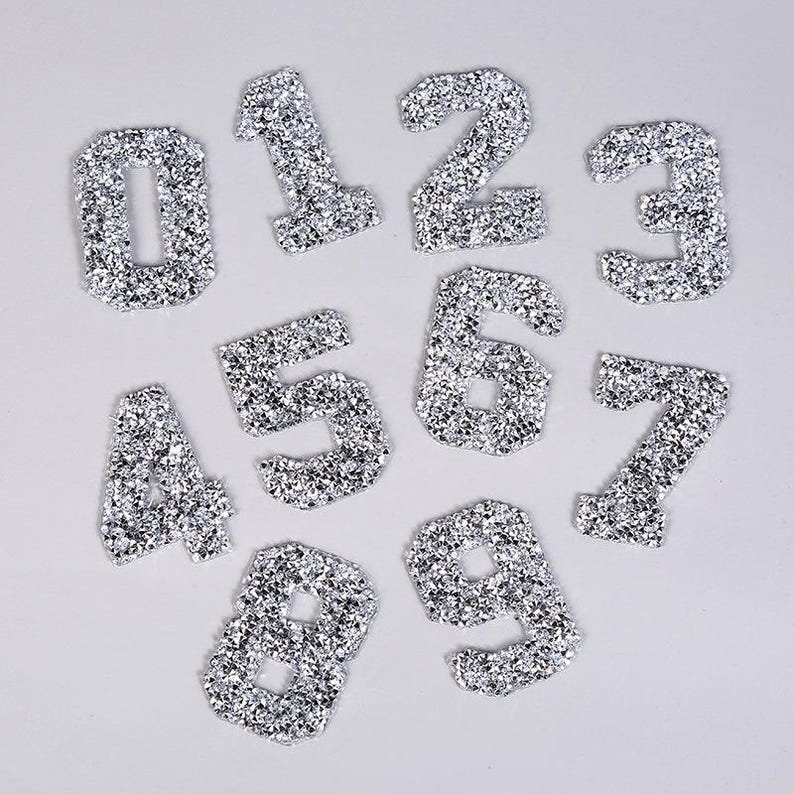 May include: Ten silver glitter iron-on patches in the shape of numbers 0 through 9.