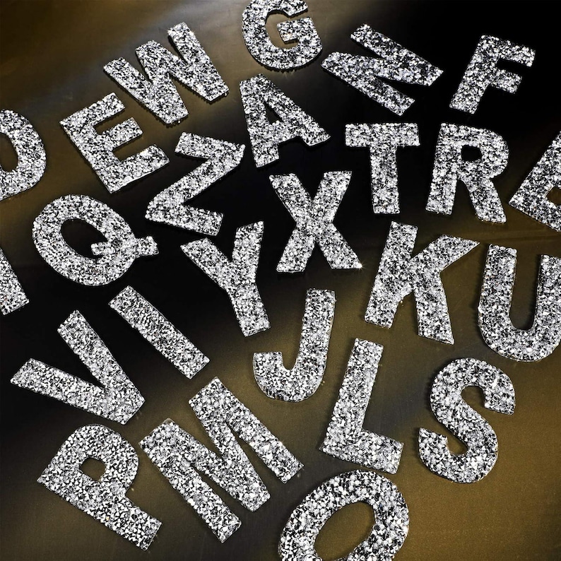 May include: A collection of silver glitter letters, including the letters A, B, C, D, E, F, G, H, I, J, K, L, M, N, O, P, Q, R, S, T, U, V, W, X, Y, and Z.
