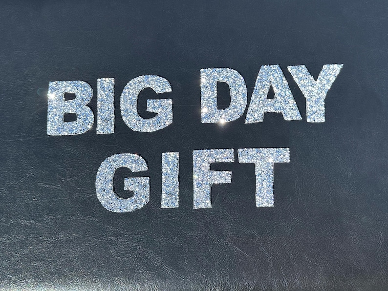 May include: A black background with the words "BIG DAY GIFT" in silver glitter letters.