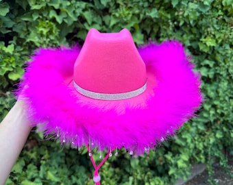 May include: A pink cowboy hat with a rhinestone band and a pink feather trim.