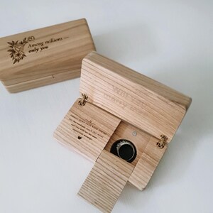 May include: A light-coloured wooden ring box, engraved with the words "Among millions - only you" and a floral design. The box opens to reveal a ring and the words "Will you marry me?" inside.