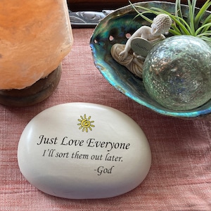 May include: White stone with a yellow sun and the text "Just Love Everyone I'll sort them out later. -God"