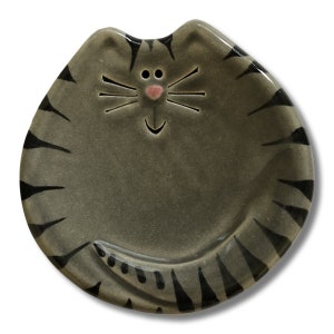 May include: A gray ceramic cat dish with black stripes and a pink nose. The dish is shaped like a cat with a smiling face.