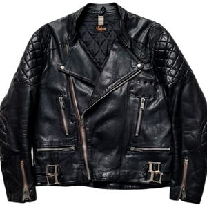 May include: Black leather motorcycle jacket with quilted shoulder and elbow padding. Features a diagonal zipper closure, multiple zippered pockets, and silver-tone hardware. The jacket has a classic biker style.