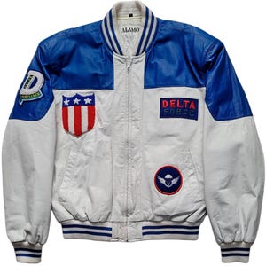 May include: White and blue bomber jacket with patches. The jacket has blue sleeves and a white body. Patches include a shield with stars and stripes, a Delta Force patch, and a patch with a parachute.