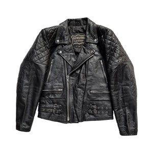 Puede incluir: Chaqueta de cuero negra para moto con hombros acolchados y cierre de cremallera. La chaqueta tiene una etiqueta que dice "Cuero genuino".