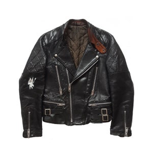 May include: Black leather biker jacket with a quilted design and a zip fastening. The jacket has a brown leather collar and a white graphic on the left sleeve.