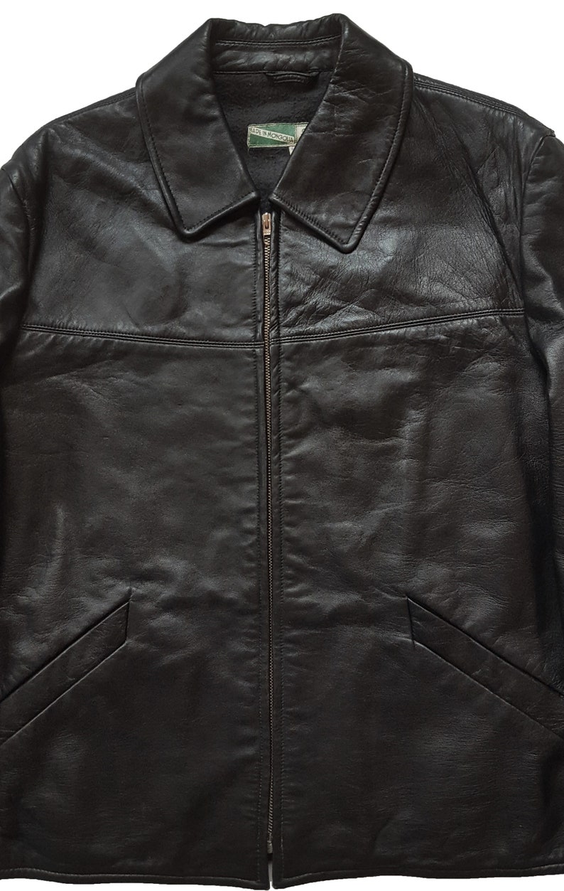 May include: A black leather jacket with a zipper closure and a collar. The jacket has two pockets on the bottom and a label that reads "Made in Mongolia".