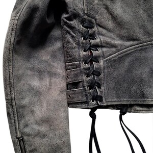 May include: A gray suede jacket with a lace-up detail on the side. The jacket has a zipper on the sleeve and a frayed hem.