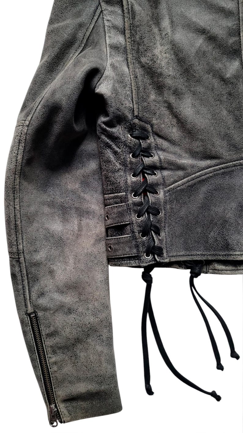 May include: A gray suede jacket with a lace-up detail on the side. The jacket has a zipper on the sleeve and a frayed hem.