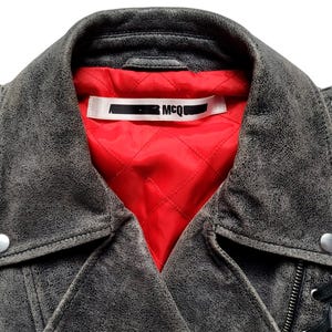 May include: A gray leather motorcycle jacket with a red quilted lining and a black label that says "MCQ" on the inside of the collar.