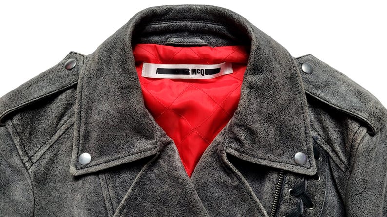 May include: A gray leather motorcycle jacket with a red quilted lining and a black label that says "MCQ" on the inside of the collar.