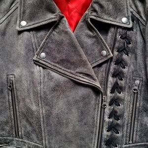 May include: A gray leather motorcycle jacket with black laces up the side, a zipper closure, and a red lining. The jacket has a label that says "MCQ".