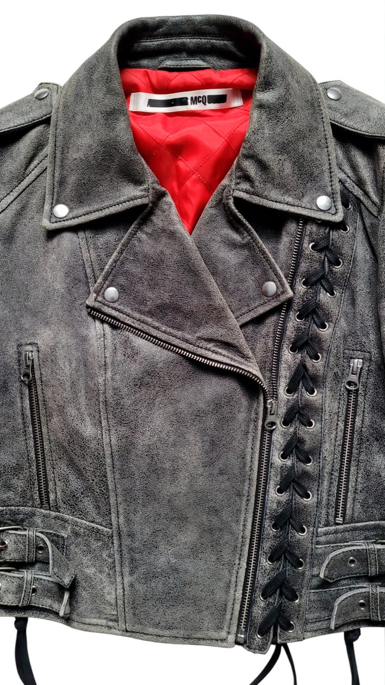 May include: A gray leather motorcycle jacket with black laces up the side, a zipper closure, and a red lining. The jacket has a label that says "MCQ".