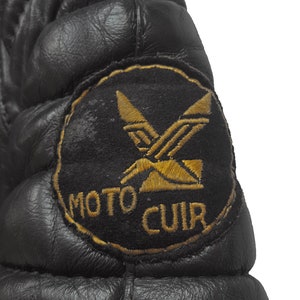 May include: Black leather jacket with a quilted design and a gold embroidered patch that says "MOTO CUIR" with a stylized X design.