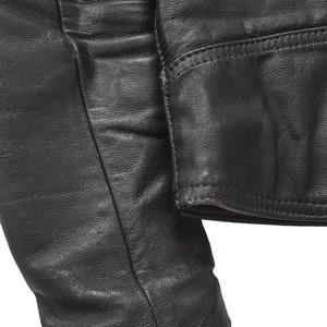 May include: Close-up of a black leather jacket sleeve with a seam detail. The sleeve is folded over and the fabric is textured.