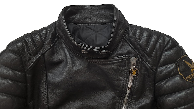 May include: Black leather motorcycle jacket with quilted shoulders and a zipper closure. The jacket has a gold zipper pull with a logo and a gold patch on the right sleeve with the text "MOTORCYCLE".