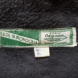 May include: A green and white label with the text "Made in Mongolia" and a smaller white label with the text "Anmay Bergmann" in black.