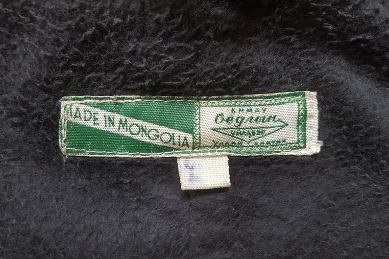 May include: A green and white label with the text "Made in Mongolia" and a smaller white label with the text "Anmay Bergmann" in black.