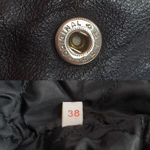 May include: Close-up of a black leather jacket with a silver button that says "Original by" and a size tag that says "38".