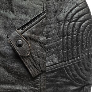 Może przedstawiać: Zbliżenie na czarną sk&oacute;rzaną kurtkę z zamkiem błyskawicznym i pikowanym wzorem na rękawie.