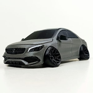 May include: A gray 3D printed model of a Mercedes-Benz car with black wheels and a black grille. The car is a coupe style with a sloping roofline.