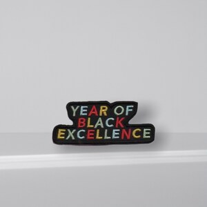 May include: Black embroidered patch with the text "YEAR OF BLACK EXCELLENCE" in rainbow colours.