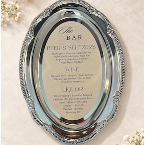 May include: An oval silver-toned metal tray with a decorative embossed border. The center features a printed menu titled The Bar, listing categories for Beer & Seltzers, Wine, and Liquor with various brand names including Bud Light, Corona, and Tito's.