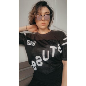 K&ouml;nnte beinhalten: Ein schwarzes Mesh-Trikot mit wei&szlig;en Buchstaben, auf dem "1981" und "Beauty" steht. Das Trikot hat wei&szlig;e Streifen an den &Auml;rmeln.